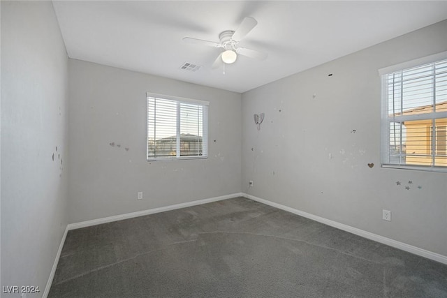 empty room featuring ceiling fan, plenty of natural light, and dark colored carpet