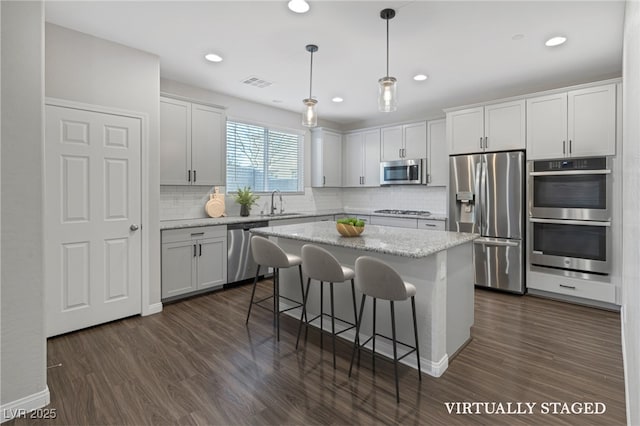 kitchen featuring pendant lighting, appliances with stainless steel finishes, white cabinets, a kitchen island, and dark hardwood / wood-style flooring