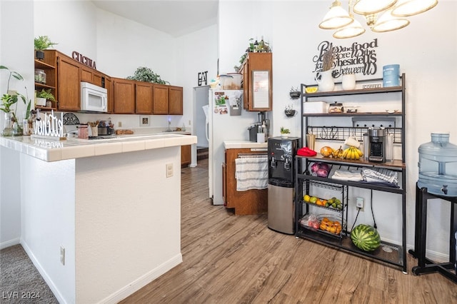 kitchen featuring pendant lighting, a notable chandelier, light wood-type flooring, tile counters, and kitchen peninsula