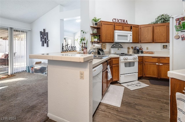 kitchen featuring sink, dark wood-type flooring, kitchen peninsula, lofted ceiling, and white appliances