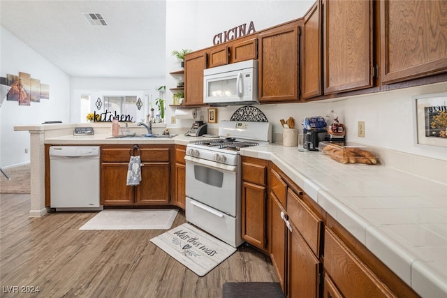 kitchen with kitchen peninsula, white appliances, sink, tile countertops, and light hardwood / wood-style flooring