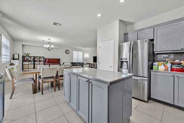 kitchen with gray cabinetry, a kitchen island, light stone counters, and stainless steel fridge with ice dispenser