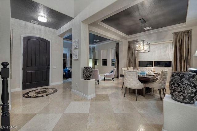 foyer entrance with an inviting chandelier, a raised ceiling, and crown molding