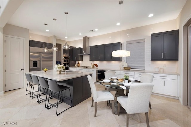 kitchen with tasteful backsplash, wall chimney range hood, pendant lighting, a breakfast bar area, and an island with sink