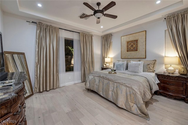 bedroom featuring ceiling fan, a tray ceiling, and light hardwood / wood-style flooring