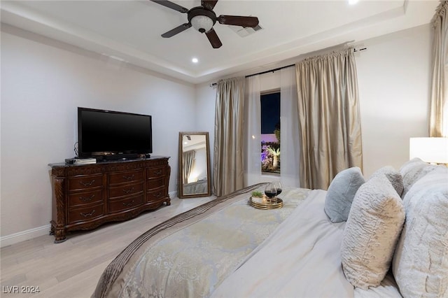 bedroom featuring light wood-type flooring, a tray ceiling, and ceiling fan