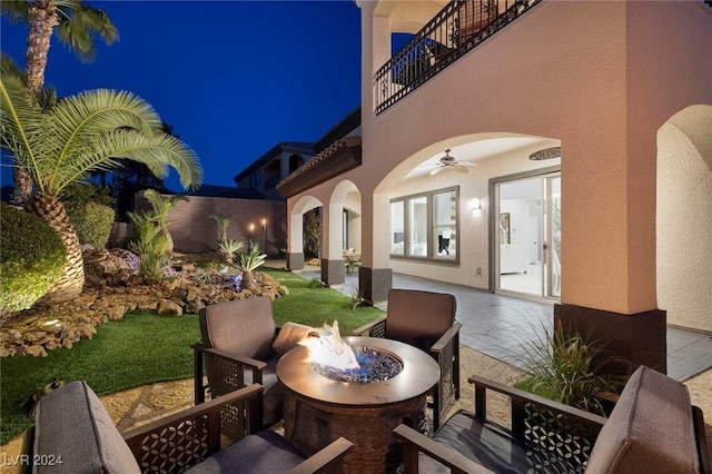 patio at night featuring ceiling fan, a balcony, and a yard