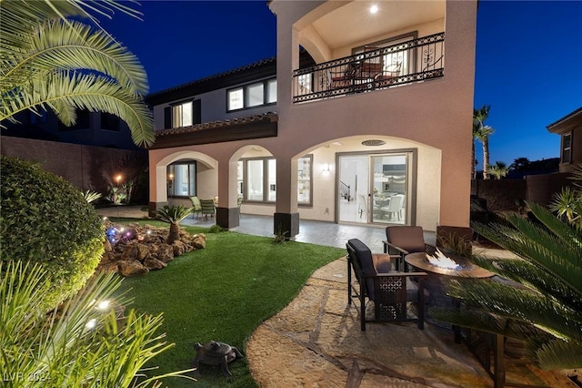 back house at twilight featuring a yard, a patio area, french doors, and a balcony