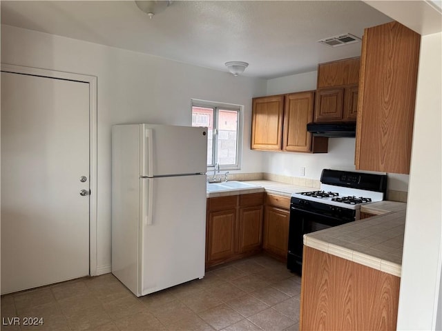 kitchen featuring black gas range oven, extractor fan, sink, tile countertops, and white fridge