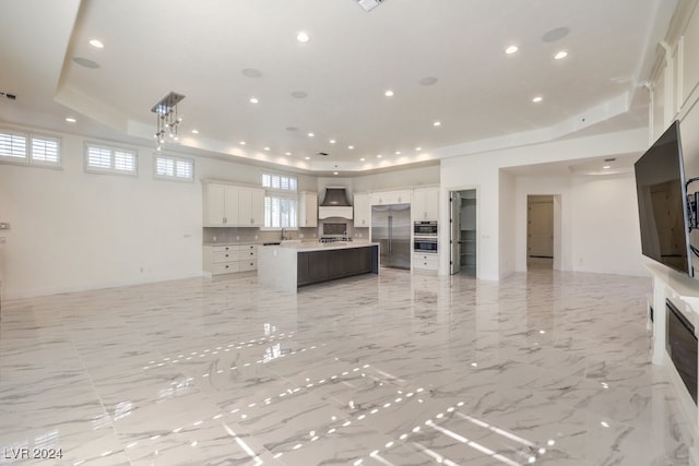 kitchen with white cabinetry, sink, a kitchen island with sink, custom range hood, and appliances with stainless steel finishes