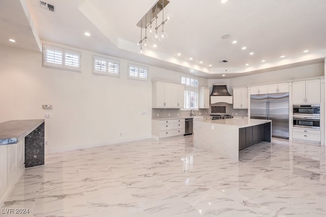 kitchen featuring white cabinets, stainless steel appliances, a raised ceiling, and an island with sink