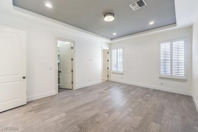 unfurnished room with plenty of natural light, light wood-type flooring, and a tray ceiling