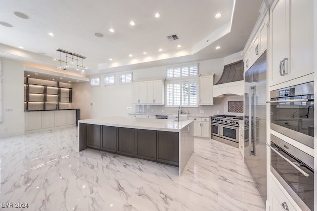 kitchen with sink, high quality appliances, white cabinets, hanging light fixtures, and an island with sink