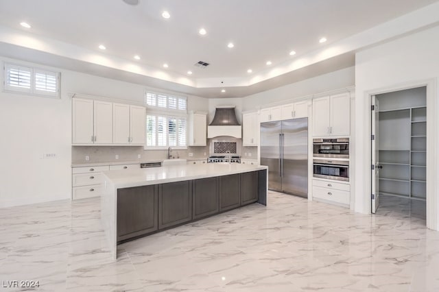 kitchen featuring white cabinetry, stainless steel appliances, premium range hood, a spacious island, and decorative backsplash