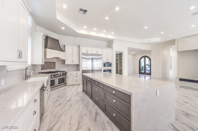 kitchen with premium appliances, white cabinetry, a spacious island, and custom range hood