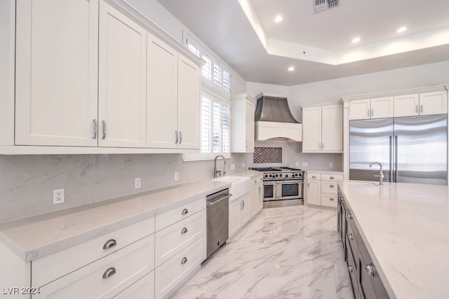 kitchen featuring light stone countertops, premium appliances, white cabinetry, and custom exhaust hood