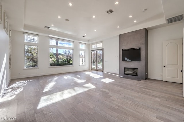 unfurnished living room featuring a tray ceiling, a large fireplace, and light hardwood / wood-style floors