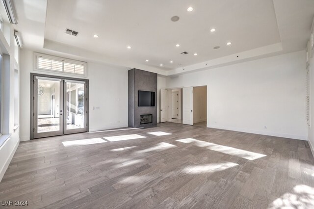 unfurnished living room featuring a large fireplace, light wood-type flooring, and a tray ceiling