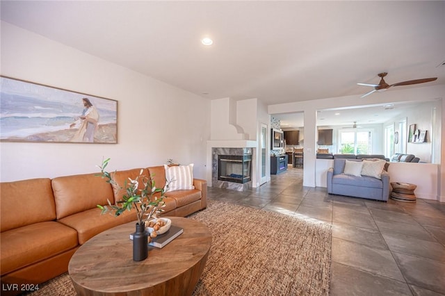 tiled living room with a high end fireplace and ceiling fan