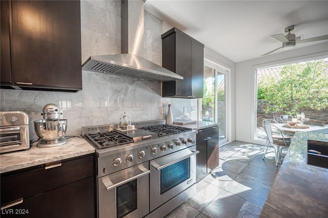 kitchen featuring dark brown cabinets, range with two ovens, wall chimney range hood, and tasteful backsplash