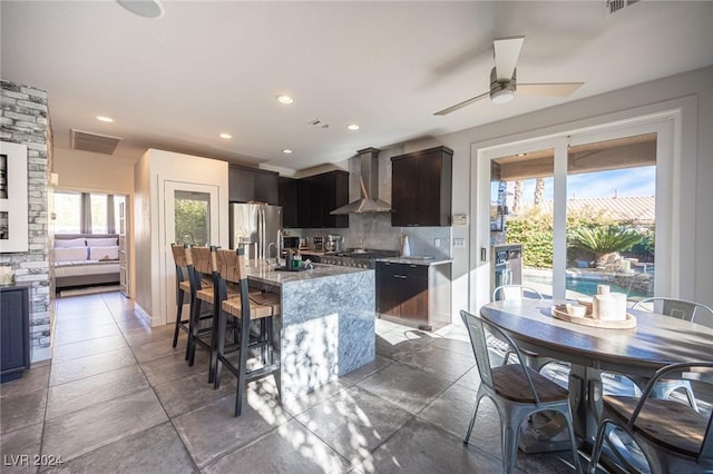 kitchen with a kitchen island with sink, plenty of natural light, wall chimney exhaust hood, and appliances with stainless steel finishes