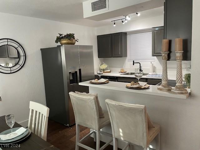 kitchen with sink, a kitchen breakfast bar, dark hardwood / wood-style floors, kitchen peninsula, and stainless steel fridge