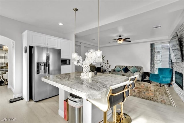 kitchen featuring white cabinetry, light hardwood / wood-style flooring, stainless steel fridge, decorative light fixtures, and a kitchen bar