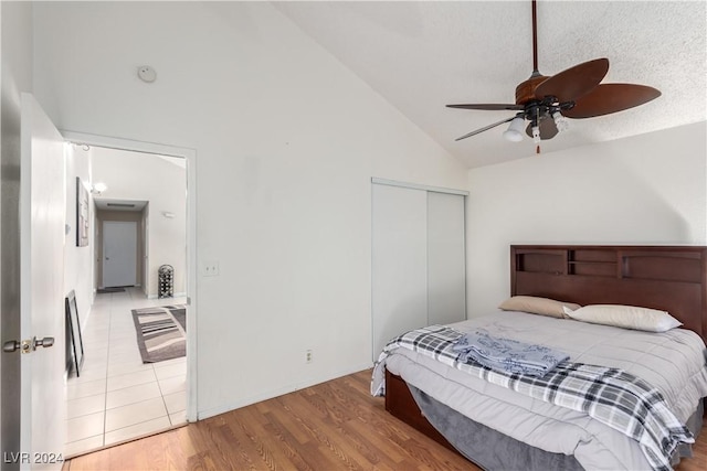 bedroom featuring high vaulted ceiling, hardwood / wood-style flooring, ceiling fan, a textured ceiling, and a closet