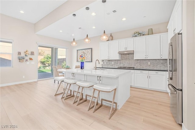 kitchen featuring an island with sink, appliances with stainless steel finishes, white cabinets, and decorative light fixtures