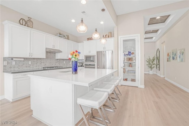 kitchen featuring pendant lighting, stainless steel appliances, an island with sink, and white cabinets