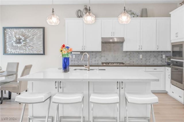 kitchen with an island with sink, sink, white cabinets, a kitchen bar, and stainless steel appliances