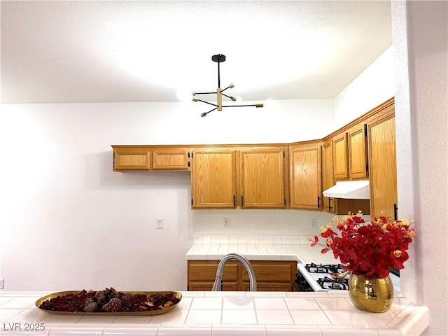 kitchen featuring sink, range, a chandelier, tile counters, and pendant lighting