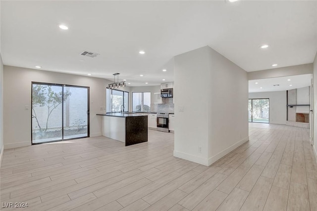 kitchen featuring decorative light fixtures, stainless steel appliances, white cabinetry, and a wealth of natural light