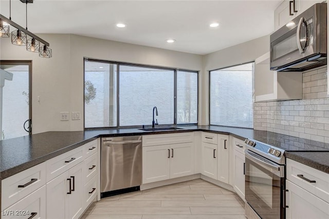 kitchen with appliances with stainless steel finishes, tasteful backsplash, sink, decorative light fixtures, and white cabinetry