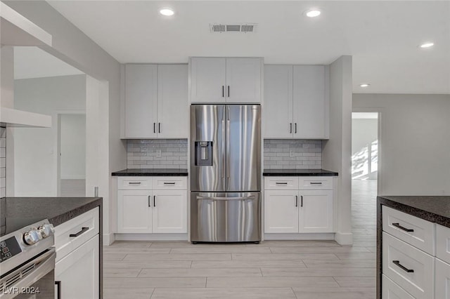 kitchen featuring stainless steel fridge, electric range oven, white cabinetry, and tasteful backsplash