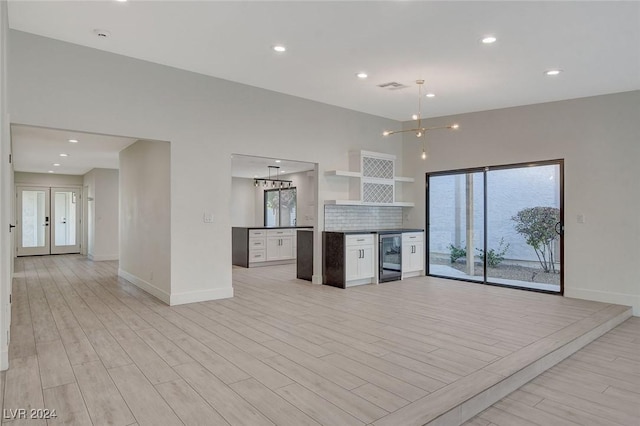 kitchen featuring white cabinetry, french doors, wine cooler, a chandelier, and decorative backsplash