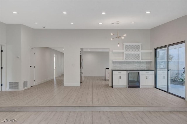 kitchen featuring backsplash, beverage cooler, decorative light fixtures, white cabinets, and stainless steel refrigerator