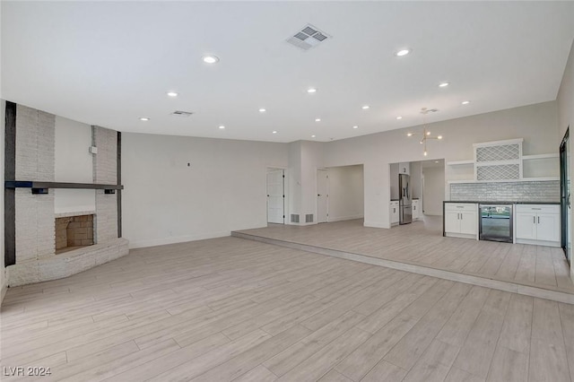 unfurnished living room featuring a fireplace, light hardwood / wood-style floors, and beverage cooler