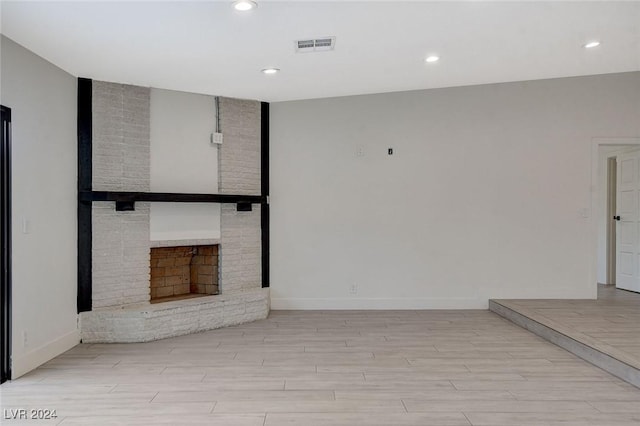 spare room with light hardwood / wood-style floors and a brick fireplace