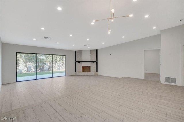 unfurnished living room with an inviting chandelier, light wood-type flooring, and a brick fireplace