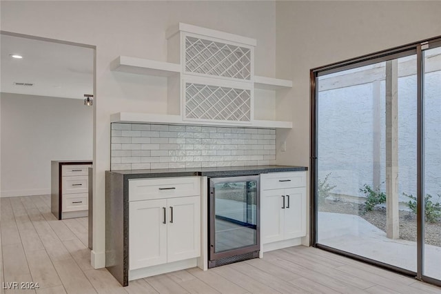 kitchen with backsplash, white cabinets, beverage cooler, and light hardwood / wood-style floors