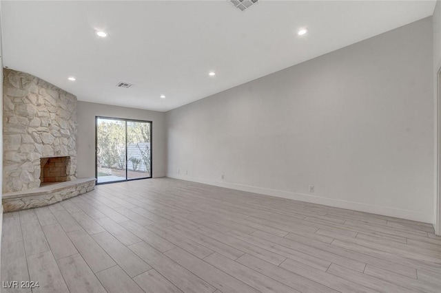 unfurnished living room featuring a stone fireplace and light hardwood / wood-style floors