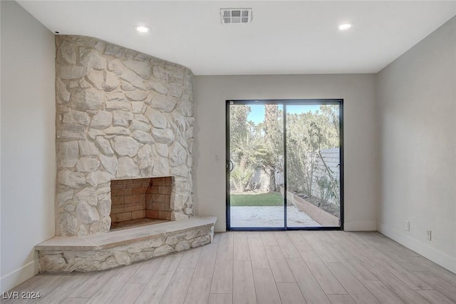 unfurnished living room with light hardwood / wood-style floors and a stone fireplace