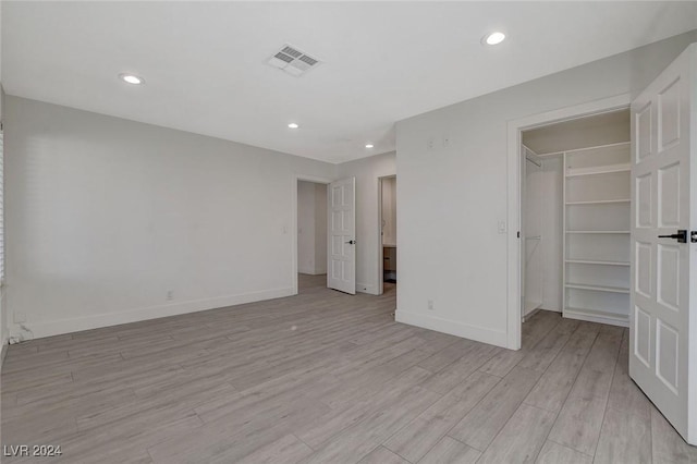 unfurnished bedroom featuring a walk in closet, a closet, and light hardwood / wood-style flooring