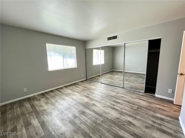 unfurnished bedroom with wood-type flooring, a textured ceiling, and a closet