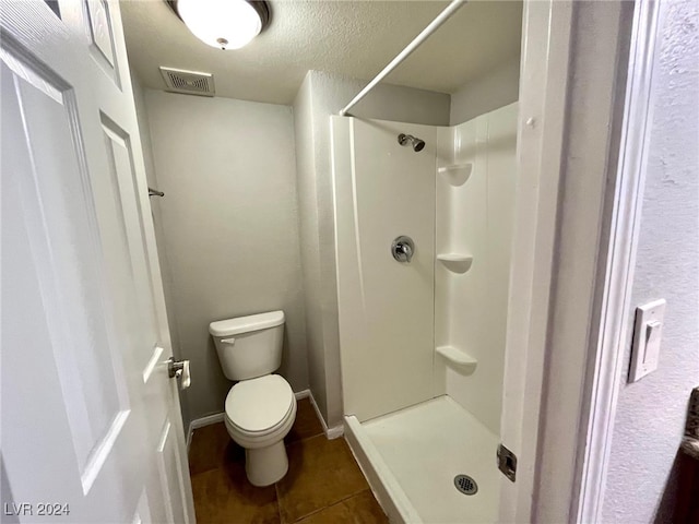 bathroom with tile patterned flooring, toilet, a shower, and a textured ceiling