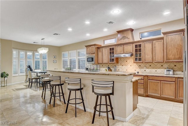 kitchen featuring stainless steel microwave, an island with sink, a chandelier, decorative light fixtures, and a kitchen bar