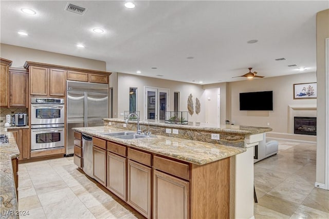 kitchen featuring light stone countertops, stainless steel appliances, ceiling fan, sink, and a large island