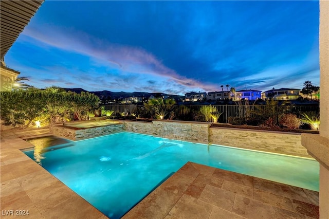 pool at dusk with pool water feature and a patio