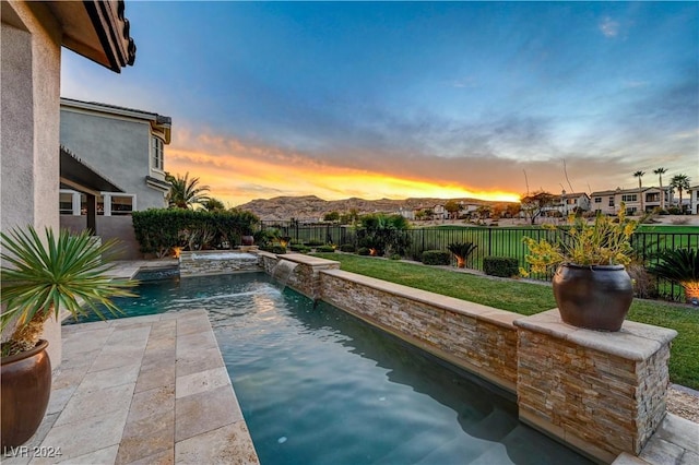 pool at dusk featuring a lawn, pool water feature, and a mountain view